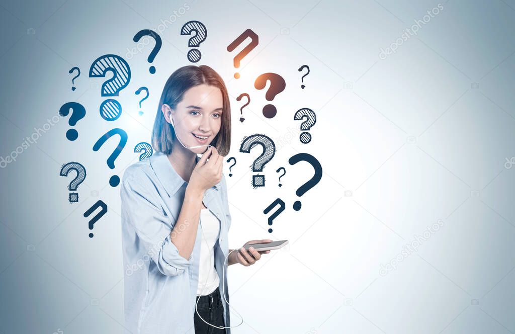 Cheerful teen girl talking on smartphone near gray wall with question marks drawn on it. Concept of communication and choice. Mock up