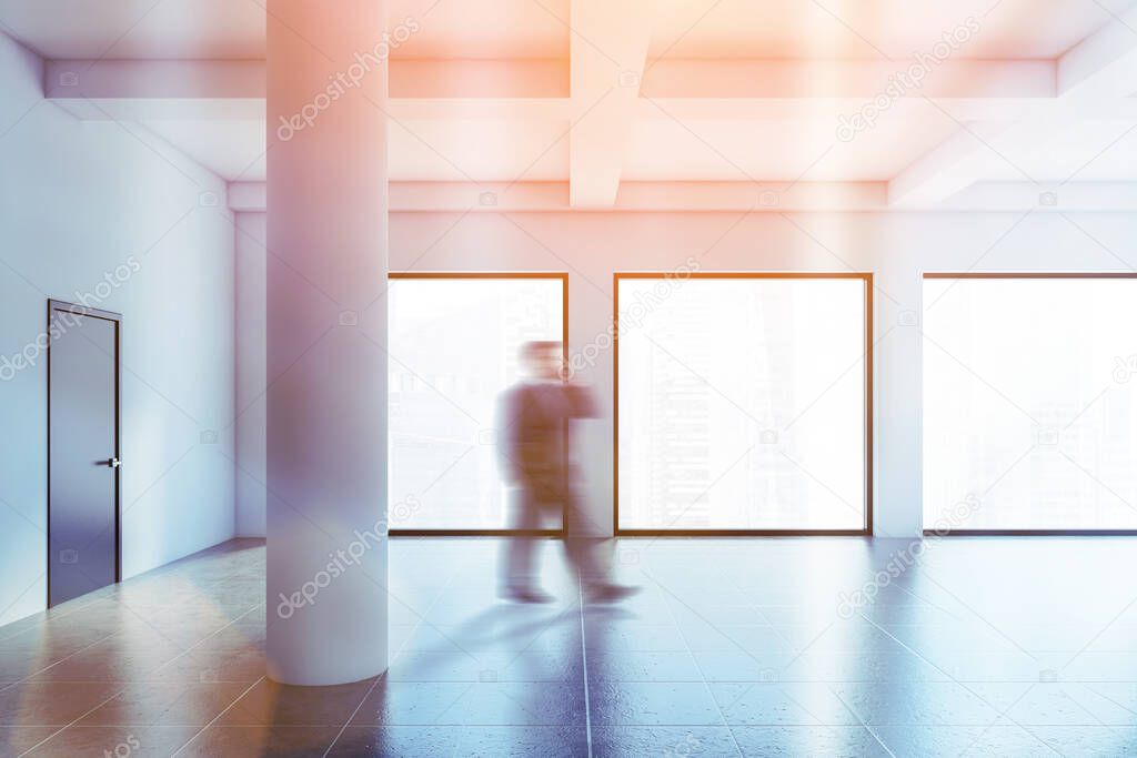 Blurry young businessman walking in empty panoramic industrial style office with white walls, columns and windows with modern cityscape. Toned image