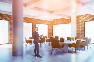 Tuğla duvarları, fayanslı zemini, turuncu sandalyeli uzun konferans masası ve bulanık şehir manzaralı kendine güvenen genç iş adamı. Tonu ayarlanmış resim