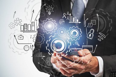 Gri duvarın yanında akıllı telefon tutan işadamlarının elleri çifte vites çizimi yapıyor. Planlama ve takım çalışması kavramı. Tonu ayarlanmış resim