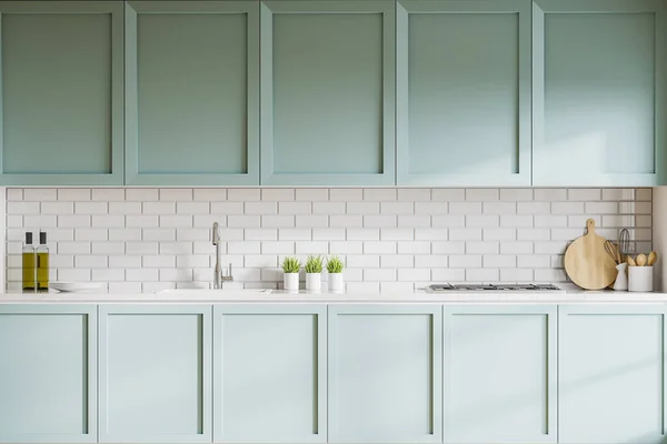 Interior of stylish kitchen with white brick walls, blue cupboards and countertops with built in sink and cooker. 3d rendering