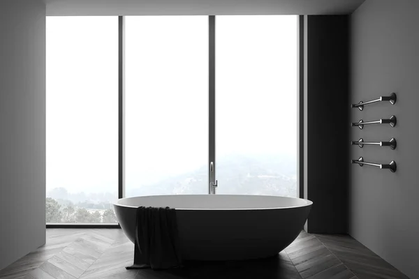 Interior of spacious bathroom with dark gray walls, wooden floor, comfortable bathtub with towel hanging on it and panoramic window with blurry mountain view. 3d rendering