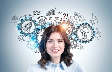 Yaratıcı vites çizimiyle gri duvarın yanında duran koyu saçlı neşeli Avrupalı genç iş kadını. Takım çalışması ve beyin fırtınası kavramı