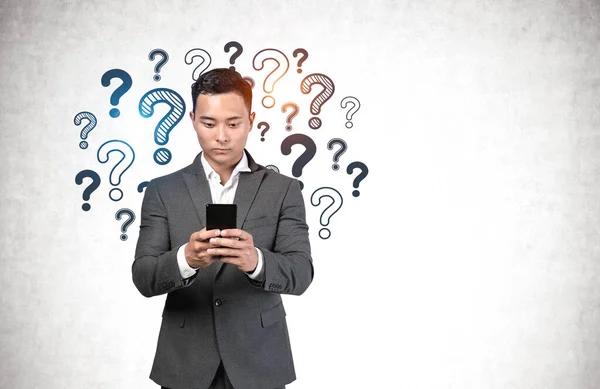 Serious Young Asian Businessman Using Smartphone Concrete Wall Question Marks — Stock Photo, Image