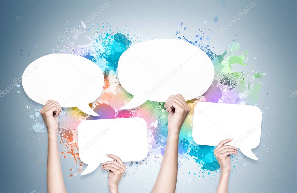 Woman hands holding blank speech bubbles over grey wall background with colorful paint splashes. Concept of communication, debate and opinion sharing. Mock up