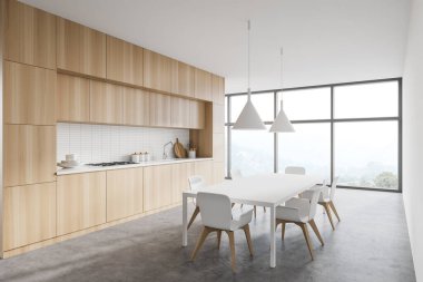 Beyaz duvarları, beton zemini, ahşap tezgahları ve dolapları olan modern mutfağın köşesi sandalyeli yemek masası ve bulanık dağ manzaralı panoramik pencere. 3d oluşturma