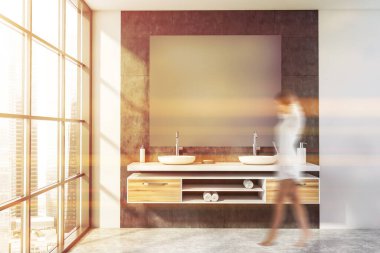 Beyaz ve gri fayanslı duvarları olan panoramik banyoda yürüyen bulanık genç kadın kare aynalı çift lavabo ve bulanık şehir manzaralı pencere. Tonu ayarlanmış resim