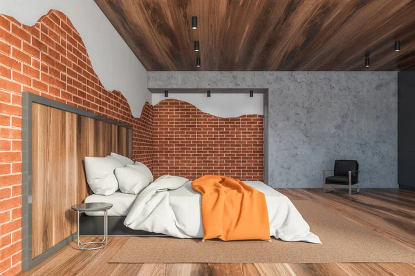 Side view of stylish loft master bedroom with white and brick walls, wooden floor and ceiling, comfortable king size bed with orange blanket and armchair. 3d rendering