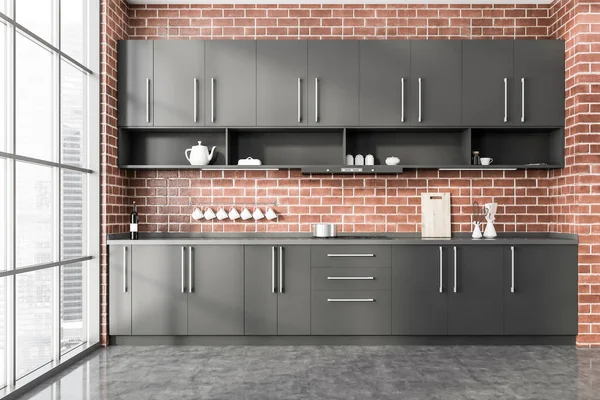 Interior of stylish panoramic kitchen with brick walls, concrete floor, gray cupboards and countertops with built in cooker. Window with blurry cityscape. 3d rendering