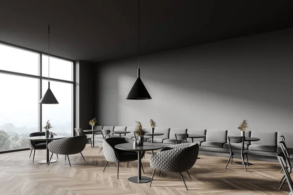 Corner of panoramic coffee shop with dark gray walls, wooden floor, cozy round tables with armchairs and comfortable long sofa. Window with blurry mountain view. 3d rendering
