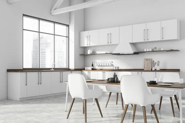 Corner of modern kitchen with white brick walls, concrete floor, white countertops and dining table with white chairs. Window with blurry cityscape. 3d rendering