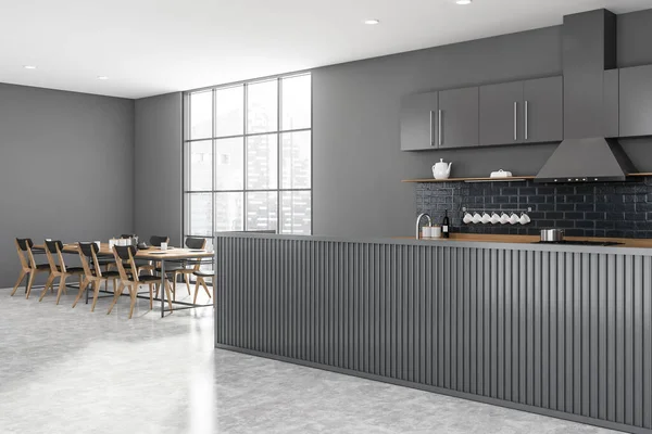 现代厨房的拐角处 有灰色的墙壁 混凝土地面 灰色的木制岛屿 长长的餐桌 靠窗的灰色椅子 城市景观模糊 3D渲染 — 图库照片
