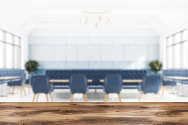 Wooden table for your product in blurry modern restaurant with white and blue walls, wooden floor, long wooden tables with blue chairs and comfortable sofas. 3d rendering mock up