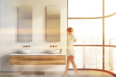 Panoramik banyoda beyaz duvarları, fayanslı zemini ve ahşap tezgahın üzerinde duran iki lavabosu olan bulanık genç bir kadın. Tonu ayarlanmış resim