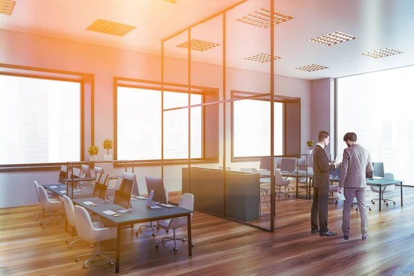 Gri duvarları, uzun bilgisayar tabloları ve büyük pencereleri olan iki iş adamı açık uzay ofisinde konuşuyor. Tonu ayarlanmış resim