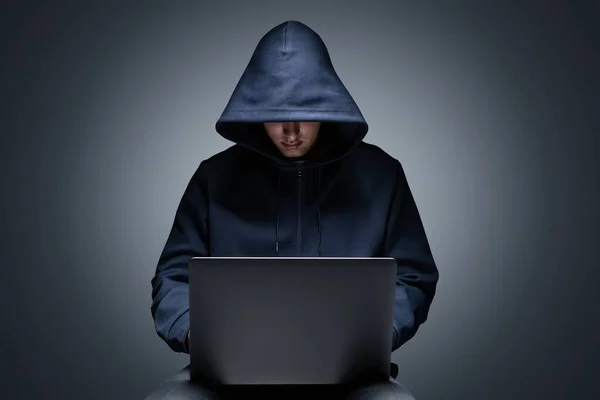 无法辨认的年轻黑客穿着黑色帽衫 用笔记本电脑在灰色墙壁背景下的肖像 网络安全和数据保护的概念 — 图库照片