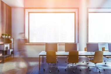 Beyaz, ahşap duvarlar ve uzun bilgisayar masasıyla açık uzay ofisinde yürüyen genç bulanık iş adamı. Tonu ayarlanmış resim