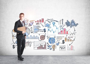 Genç Avrupalı işadamı beton duvarın yanında duran ve üzerine iş çizimi çizilmiş bir pano ile.