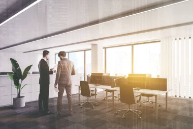 Açık uzay ofisinde beyaz duvarları, halı döşemeleri ve sıra sıra bilgisayar masalarıyla konuşan iki genç iş adamı. Renkli resim çift pozlama
