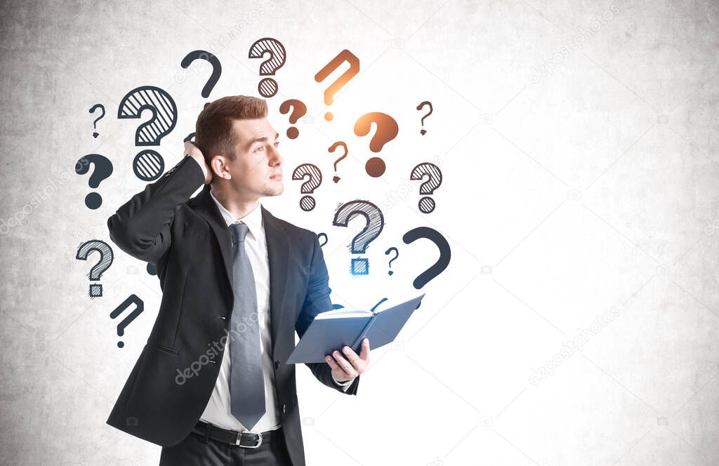 Confused young businessman standing with notebook near concrete wall with question marks drawn on it. Mock up