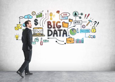 Sakallı genç işadamı üzerine renkli büyük bir veri çizimi yapılmış beton duvarın yanında yürüyor.