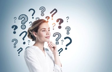 Üzerinde soru işaretleri olan gri duvarın yanında duran düşünceli genç Avrupalı iş kadını. Model