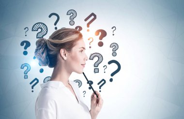 Üzerinde soru işaretleri olan gri duvarın yanında duran düşünceli genç iş kadını. Model