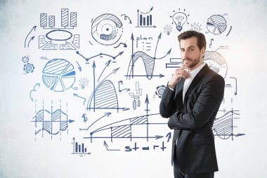 Üzerinde çizimler olan beton duvarın yanında duran düşünceli genç sakallı iş adamı.