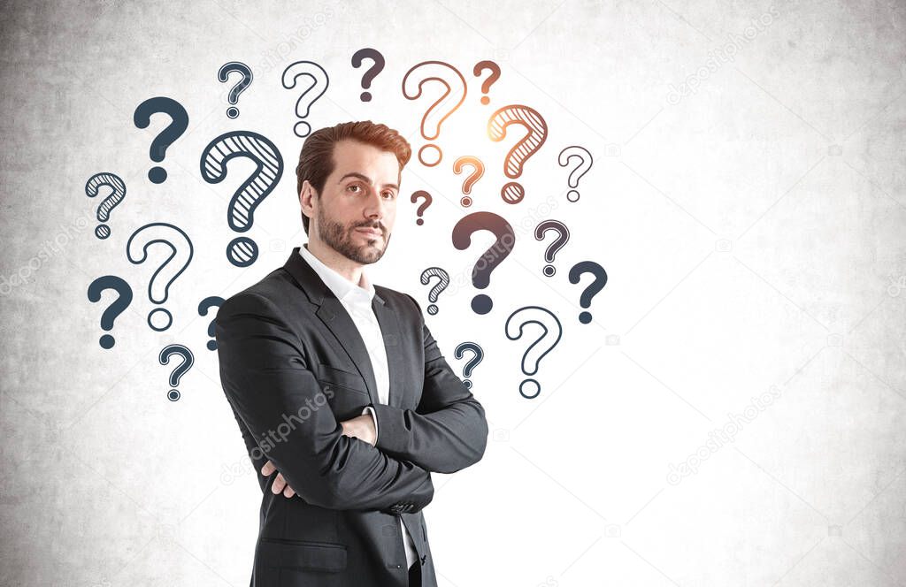 Portrait of confident bearded businessman standing with crossed arms near concrete wall with question marks drawn on it. Mock up