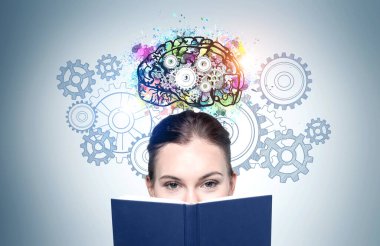 Kitapları olan genç bir iş kadını gri duvarın yanında dikiliyor..