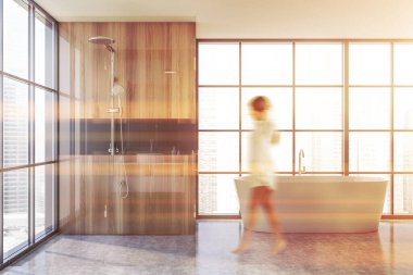 Bulanık genç bir kadın modern banyoda ahşap ve gri duvarlar, beton zemin, küvet ve duş kabini ile yürüyor. Tonu ayarlanmış resim