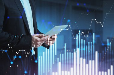 Tanımlanamayan işadamı bulanık ofiste tablet kullanıyor ve dijital tabloları iki kez gösteriyor. Tonu ayarlanmış resim