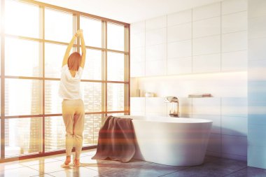 Panoramik mutfakta beyaz duvarları, fayanslı zemini ve rahat küveti olan genç bir kadının dikiz manzarası. Tonu ayarlanmış resim