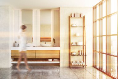 Bulanık genç bir kadın modern banyoda beyaz duvarlar, çift lavabo ve raflarla yürüyor. Tonu ayarlanmış resim