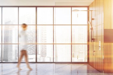 Modern banyoda tahta ve gri duvarları, beton zemini ve duş kabini olan bulanık genç bir kadın yürüyor. Tonu ayarlanmış resim