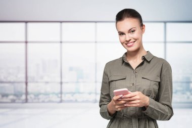 Bulanık panoramik ofiste akıllı telefon kullanan neşeli Avrupalı genç bir iş kadını. İletişim kavramı.