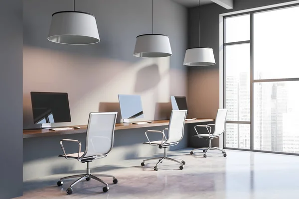 Corner of stylish open space office with gray walls, concrete floor and long wooden computer table with white chairs. Window with blurry cityscape. 3d rendering