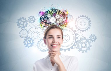 Üzerinde renkli beyin çizimi olan gri duvarın yanında duran neşeli genç iş kadını. Beyin fırtınası kavramı