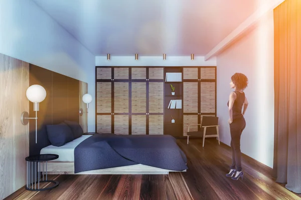 白と木製の壁 木製の床と快適なキングサイズベッド付きのモダンなベッドルームに立つ美しい若いアフリカ系アメリカ人女性 トーン画像 — ストック写真