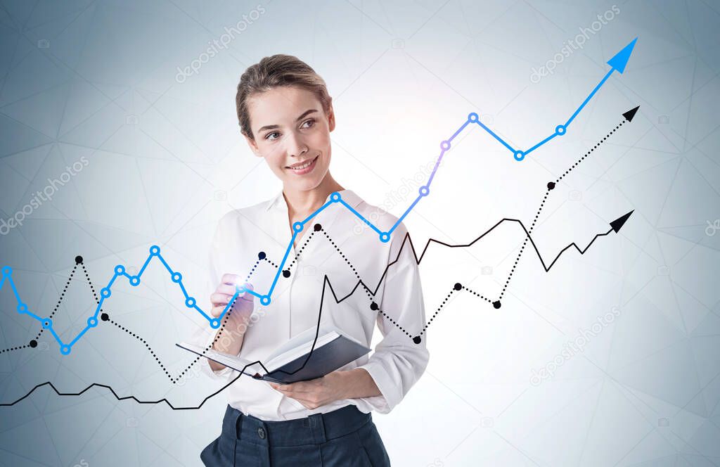 Cheerful young businesswoman standing with notebook near gray wall with growing graphs drawn on it. Concept of investment and success