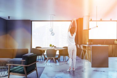 Modern mutfakta gri ve ahşap duvarları, mermer zemini ve yemek masası olan genç bir kadının dikiz görüntüsü. Tonu ayarlanmış resim