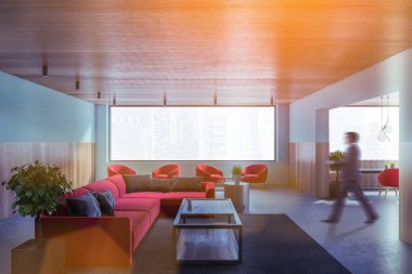 Bulanık genç adam modern yemek odasında mavi ve ahşap duvarlarla beton zemin ve kırmızı koltuklu yemek masalarıyla yürüyor. Tonu ayarlanmış resim