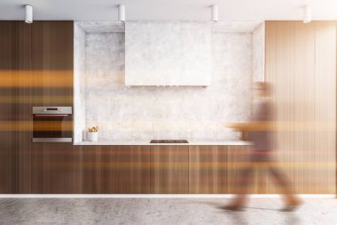 Bulanık genç adam modern mutfakta beyaz ve koyu ahşap duvarlar, beton zemin ve dolaplarla yürüyor. Tonu ayarlanmış resim