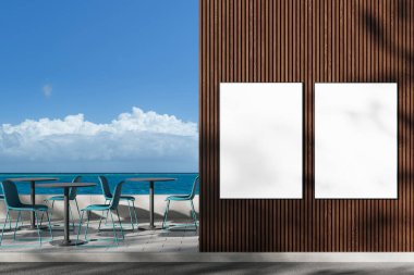 Açık bir gökyüzünün altında mavi sandalyeler ve masalarla okyanus kıyısındaki verandanın yanındaki ahşap panel cephesinde iki boş ilan panosu. 3B Hazırlama
