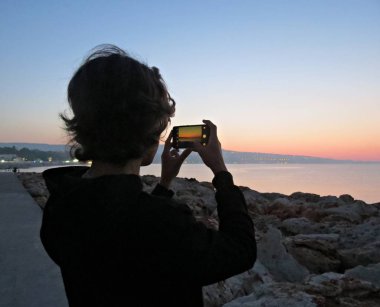 Denizde gün batımını vuran genç bir siluet. Denizde gün doğumuna bakan genç adam.