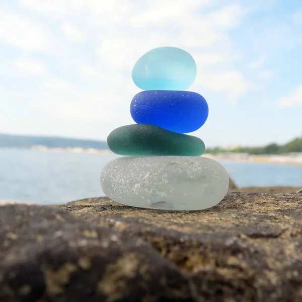 Színes tengeri üveg piramis a strandon szikla a tengeri panorámával. Sirlass verem strand hullámzó — Stock Fotó