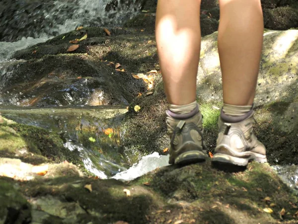Πρόσωπο με μπότες πεζοπορίας στέκεται σε μια πέτρα κοντά σε ένα ορεινό ρεύμα. Εξωτερική έννοια του τρόπου ζωής ταξίδια. Οπίσθια εικόνα. — Φωτογραφία Αρχείου