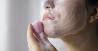 Kadın yüz masajı yapıyor. Yüz fırçası ve köpüklü temizleyici kullanıyor..