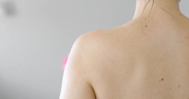 Молодая здоровая женщина стирает плечо пеной с помощью люфы, вид сзади . — стоковое видео