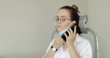 Maskeli genç bayan ofiste akıllı telefondan konuşuyor..